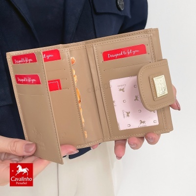 Carteira feminina bege de pele aberta com cartões vermelhos e placa metálica, segurada por pessoa com casaco azul