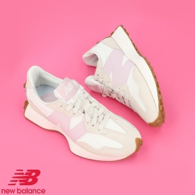 Ténis New Balance branco e rosa claro sobre fundo rosa com logótipo New Balance.