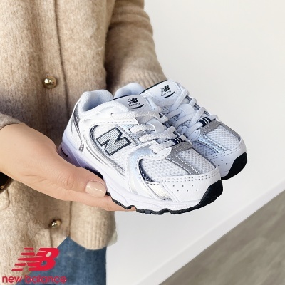 Sapatilhas infantis New Balance branco e prateado em mão de pessoa com casaco bege