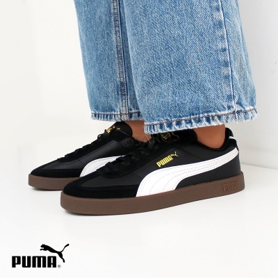 Ténis Puma preto e branco com sola castanha e calças de ganga azuis claras.