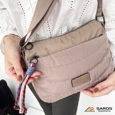 Mala pequena nude acolchoada com faixa de ombro e detalhe colorido pendurado, usada por uma pessoa.