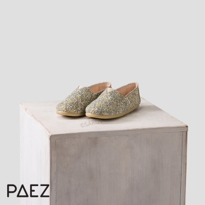 Par de alpercatas infantis com padrão floral dourado sobre cubo cinza