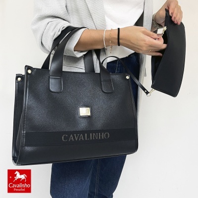 Bolsa preta de pele sintética com nome CAVALINHO em relevo e um pequeno estojo preto, segurada por uma pessoa.