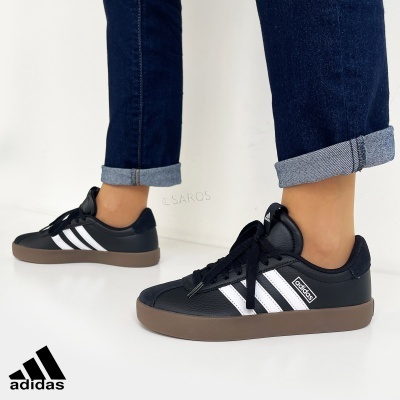 Ténis Adidas pretos com riscas brancas e sola castanha, usados com calças de ganga azul escuro