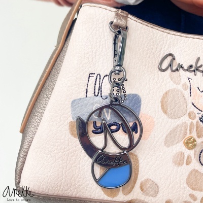 Bolsa bege com padrão manchas castanhas e chaveiro azul com marca Anekke