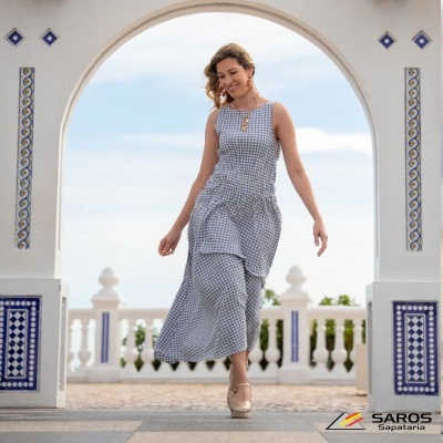 Vestido comprido xadrez azul e branco com sapatos de salto bege em cenário exterior com arco e azulejos.