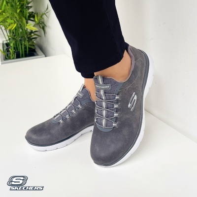 Sapatos Skechers cinza escuro com sola branca e logo visível num ambiente interno