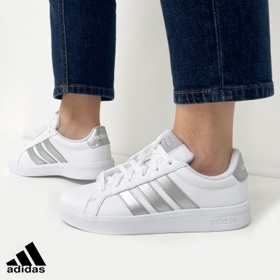 Ténis adidas brancos com riscas prateadas usados com calças de ganga