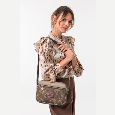 Mulher com blusa estampada, calças castanhas e mochila de ombro texturizada verde-oliva