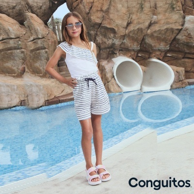 Menina jovem perto de piscina com roupa riscada azul e branca e sandálias cor-de-rosa