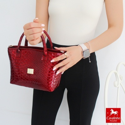Mala de mão vermelha texturizada tipo pele de crocodilo em mãos femininas
