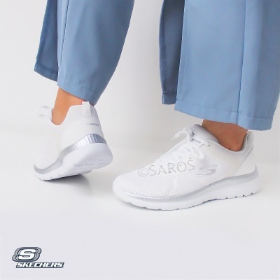 Ténis brancos Skechers usados com calças azuis claras, fundo branco.