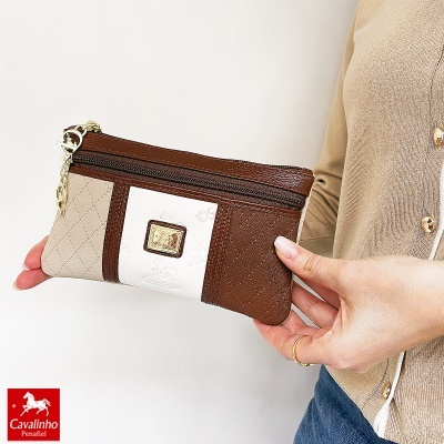 Carteira Cavalinho castanha, bege e branca com textura e logotipo dourado, segurada à mão.