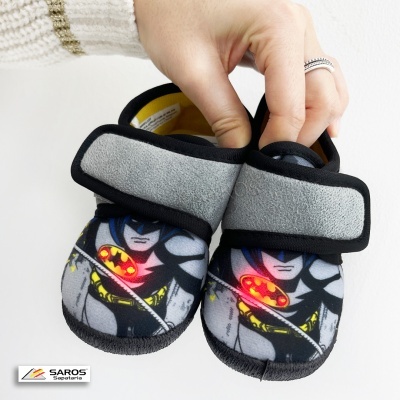 Sapatilhas infantis Batman com velcro cinzento e preto, mostradas por uma mão sobre fundo branco