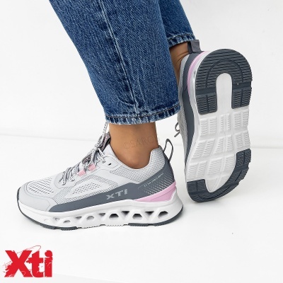 Ténis de homem XTI cinza com rosa e branco, sola alta com detalhes vazados, usado com calças de ganga azuis