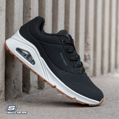 Ténis Skechers pretos contra fundo de cimento cinzento