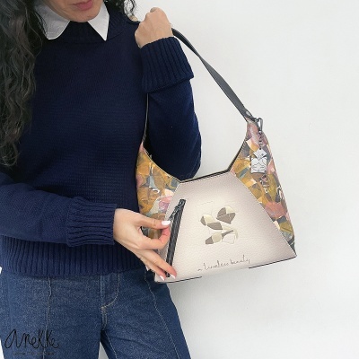 Mala feminina colorida com alça preta mostrada por modelo em camisola azul escuro