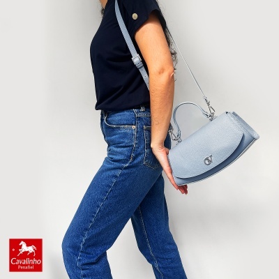 Mulher de lado com mala azul clara de pele e jeans