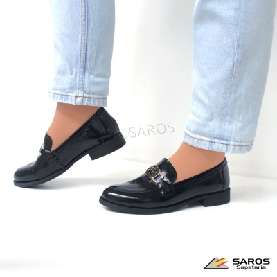 Mocassins pretos de couro brilhante com fivela dourada e calças jeans claras