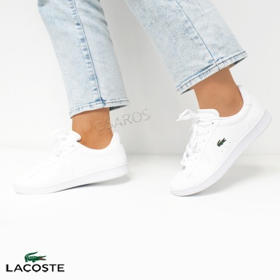 Sapatilhas brancas Lacoste com logo verde usadas com calças de ganga claras