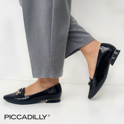 Sapatos rasos de verniz preto com detalhe dourado e fivela decorativa, usados com calças cinzentas.