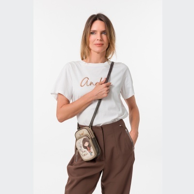 Mala pequena de tiracolo bege com padrão e desenho, usada por mulher com calças castanhas e t-shirt branca