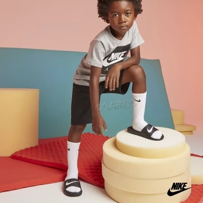 Criança com roupa Nike cinza, preta e branca e chinelos Nike