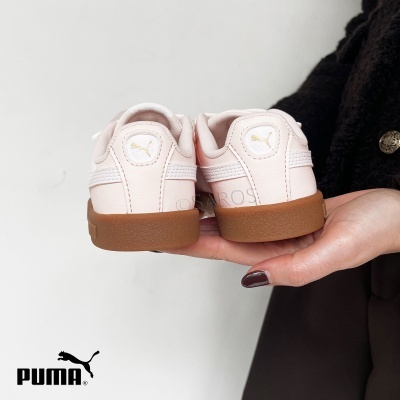 Sapatilhas Puma rosa claro com sola castanha seguradas por uma mão.