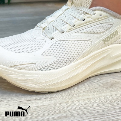 Ténis desportivos brancos Puma com malha respirável e sola espessa em chão de madeira.
