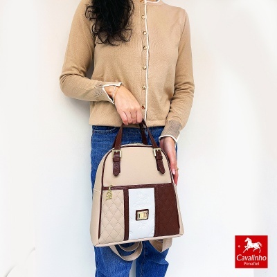 Mala de mão bicolor bege e castanho com textura matelassé, segurada por pessoa com camisola bege e jeans azuis