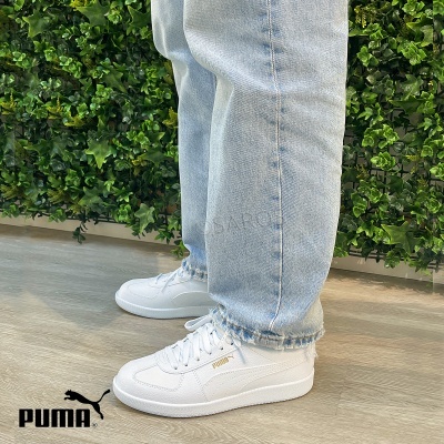 Ténis brancos Puma com logótipo dourado usados com calças de ganga