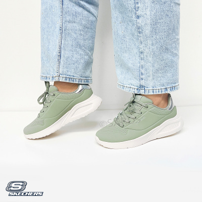 Ténis verdes Skechers com sola branca e detalhe prateado usados com jeans azul claro