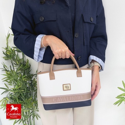 Mala Cavalinho branca, castanha e azul-marinho com alças castanhas num ambiente com plantas