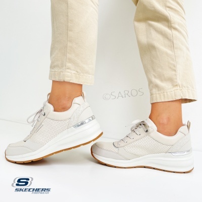 Ténis Skechers bege claro com sola branca e detalhes prateados, usados por pessoa com calças bege num fundo branco