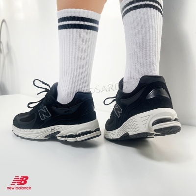 Ténis New Balance 2002R pretos com sola branca usados com meias brancas com riscas pretas