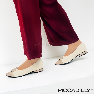 Sapatilhas de couro branco e bege com detalhe metálico, usadas com calças vermelhas.