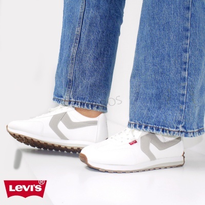 Sapatilhas brancas com detalhes cinza e etiqueta Levi's vermelha, usadas com jeans azuis