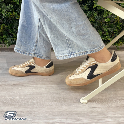Ténis Skechers creme e preto com sola castanha em ambiente interior com chão madeira clara