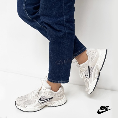 Ténis desportivos Nike bege e branco com detalhes pretos, usados com jeans.