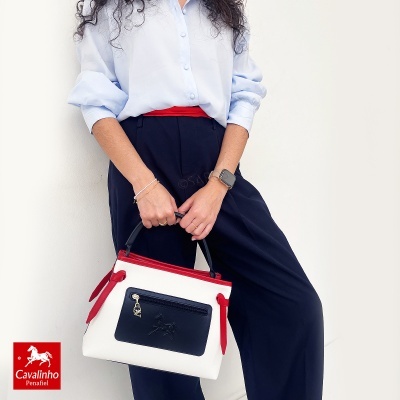 Bolsa quadrada branca com detalhes vermelhos e bolso preto de mulher com camisa azul e calças pretas
