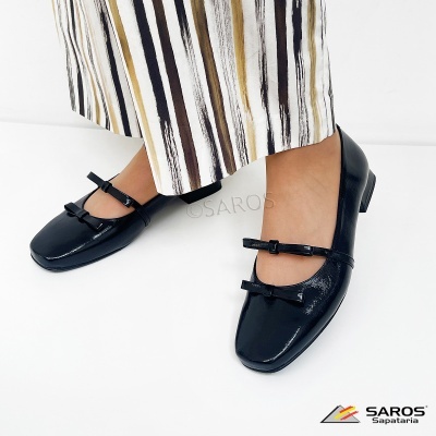 Sapatos pretos de verniz com salto baixo e laços, usados com saia ou calças riscas verticais