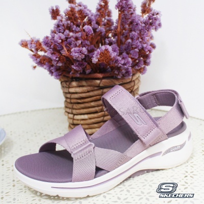 Sandália lilás da marca Skechers com tiras de tecido e sola branca perante vaso de flores lilases.