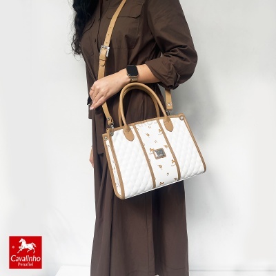 Mala de senhora branca e castanha com padrão Cavalinho e alças castanhas, usada por mulher com vestido castanho