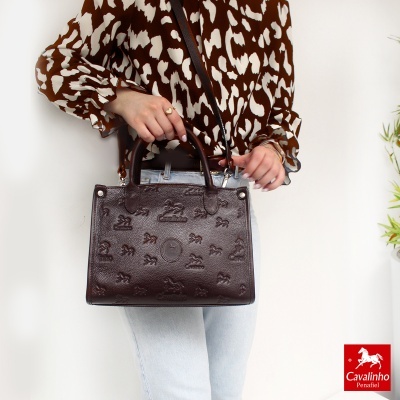 Mala de mão em pele castanha com relevo de cavalos e texto Cavalinho