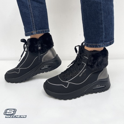 Botas pretas Skechers com pelúcia na gola e sola preta, usadas com calças de ganga