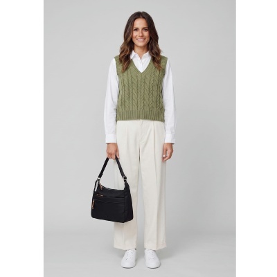 Mulher com camisola de malha verde, camisa branca, calças creme, sapatilhas brancas e mala preta
