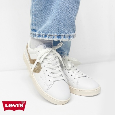 Ténis Levis brancos com detalhes dourados e jeans azuis