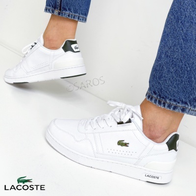 Sapatilhas Lacoste brancas com detalhes verdes e logo do crocodilo, usadas com jeans azuis.