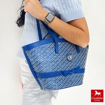 Mala de mão azul e branca com padrão entrelaçado e detalhes em pele, com laço e logotipo CV.