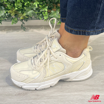 Sapatilhas New Balance 530 bege e creme com sola branca, usadas com jeans.